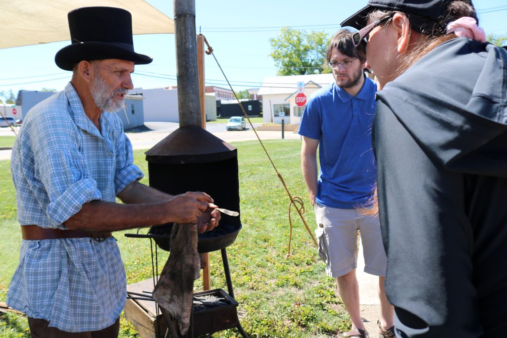 Blacksmith Station Image 4: the blacksmith is showing the piece of metal he's been working on to the surrounding crowd of people.